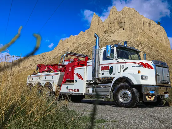 Don's heavy wrecker in tall grass below sandstone cliffs