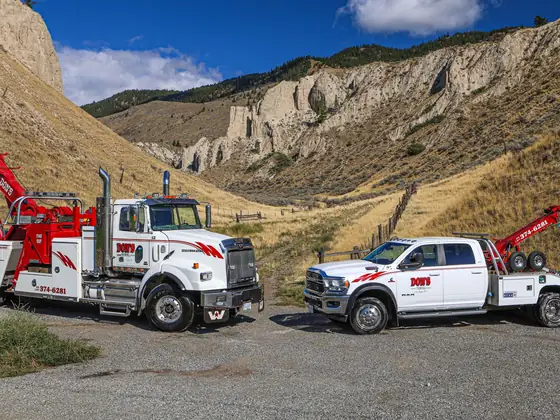 Two Don's wreckers in a gravel lot below sandstone cliffs