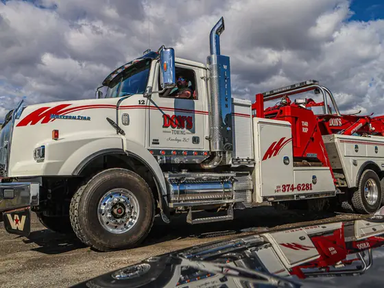 Side view of a Don's heavy wrecker reflected in a car's hood