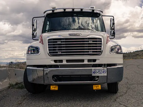 Front view of a Don's medium-duty tow truck parked by a highway barrier