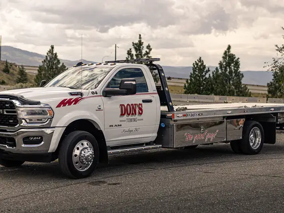 Side view of a Don's Ram flatbed tow truck under pine trees