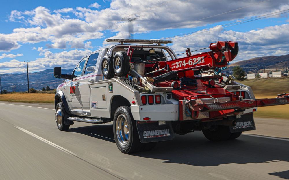 A Don's Towing wheel-lift truck driving down a highway outside Kamloops